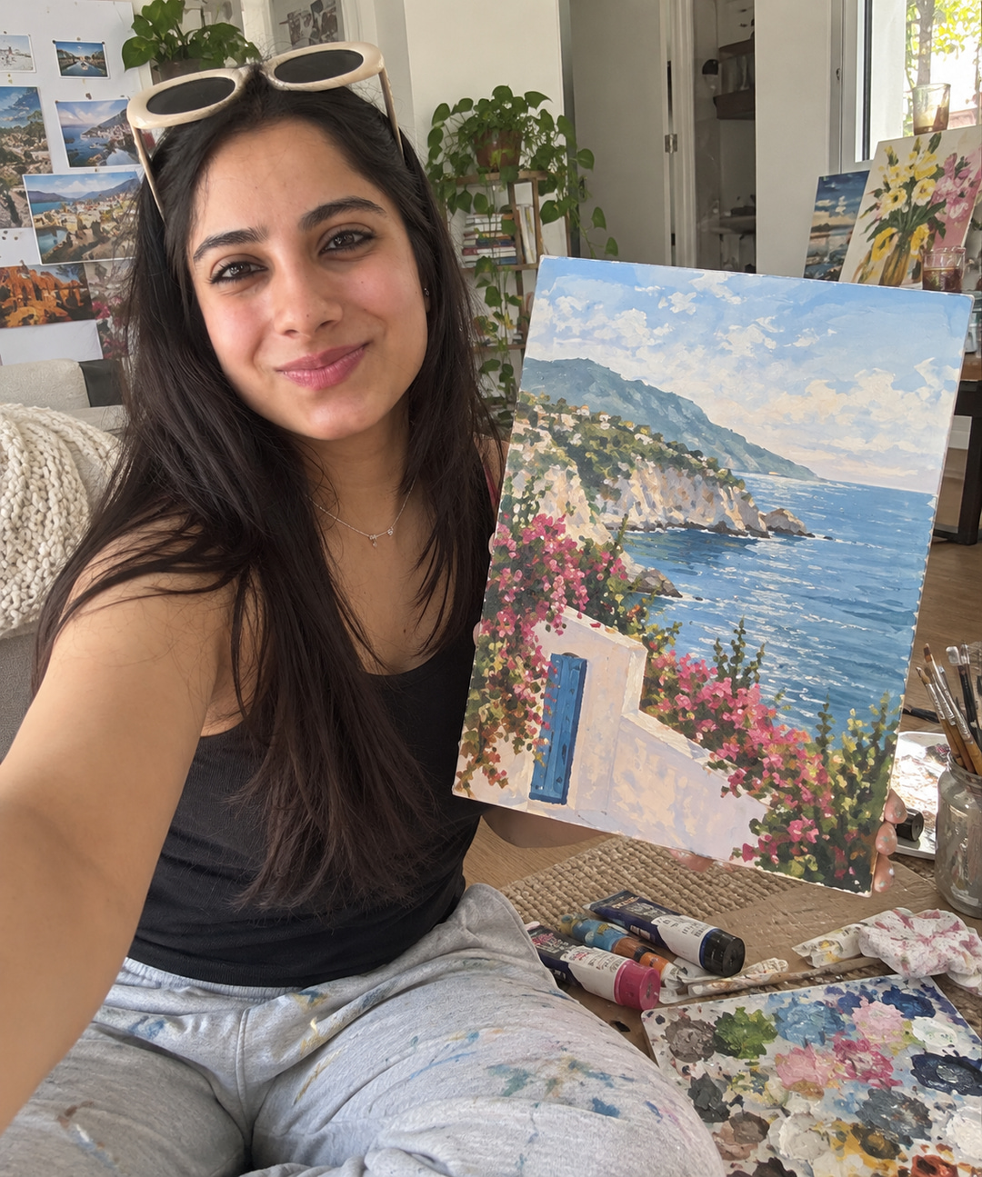 Shalini holding up a finished painting of a sea cliff and flowers